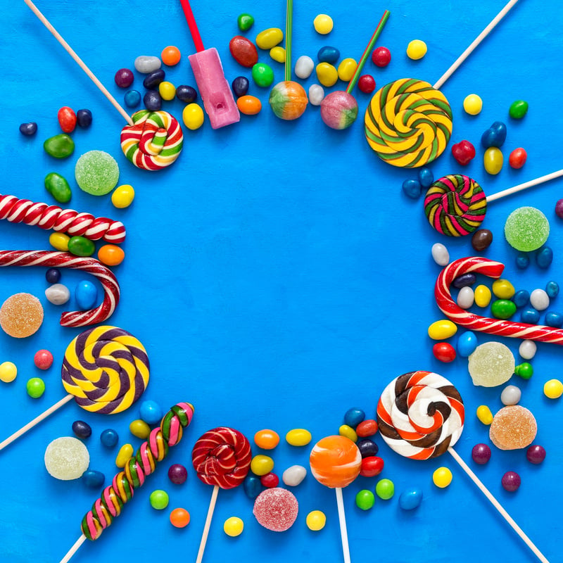 Colored candies, lollipops and marmalade on a blue background round frame. Top view, flat lay.